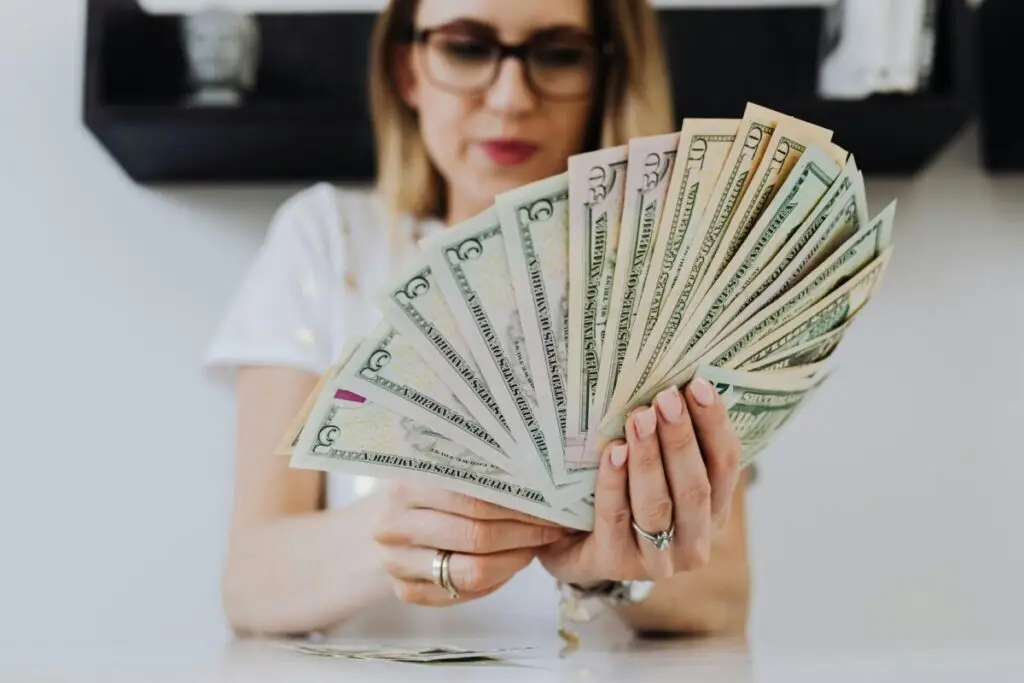 Close-up of a woman holding and fanning U.S. dollar bills indoors.