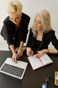 Two professional women working together on a laptop and notebook in an office setting.