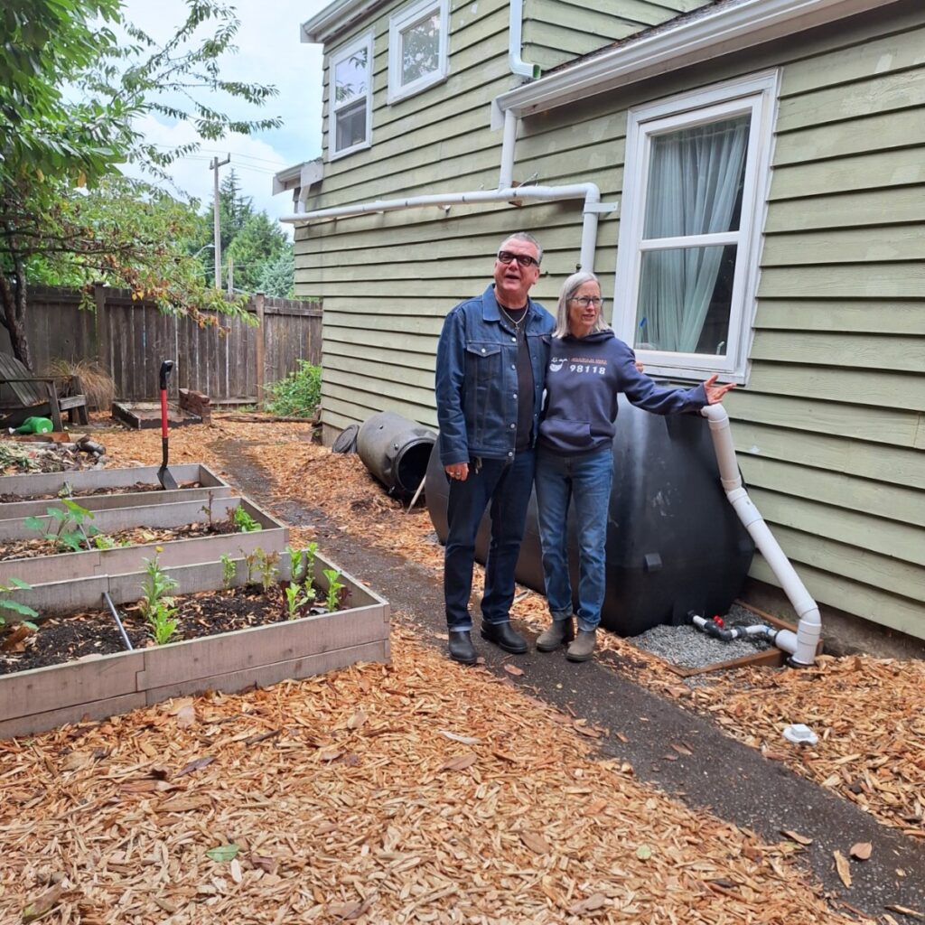 A residential home with a large rainwater collection tank installed in the yard, showing how homeowners Sarah and Mike participated in their city's RainWise program to combine environmental consciousness with financial savings through municipal rebates and stormwater managemen