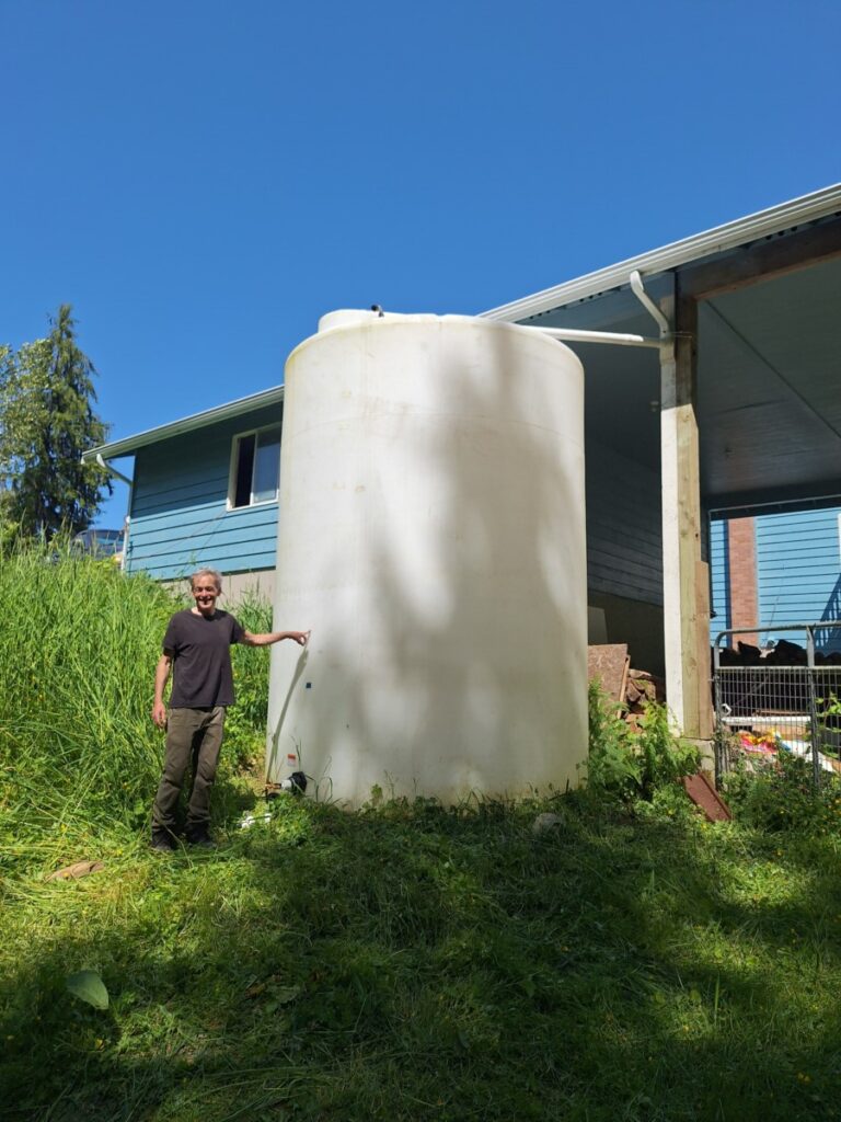 Person standing next to a large black plastic water tank in Seattle, part of an advanced rainwater harvesting system designed for sustainable water storage and efficient rainwater collection.
