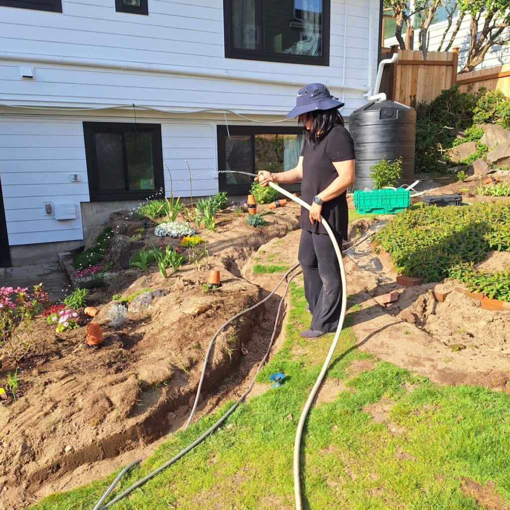 Homeowner watering a lush garden using rainwater collected from Product Water’s sustainable rainwater harvesting system outdoors