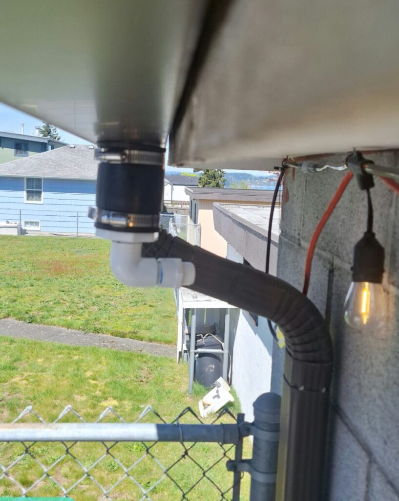 Close-up of the Product Water Deviator gutter insert redirecting rainwater horizontally from a gutter into interconnected rain tanks, enabling flexible and efficient rainwater harvesting without overflow.