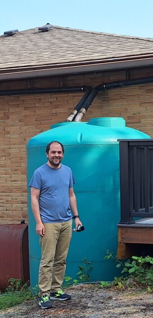 South Seattle homeowner stands proudly in front of a large rainwater tank, demonstrating sustainable water solutions for pool maintenance.